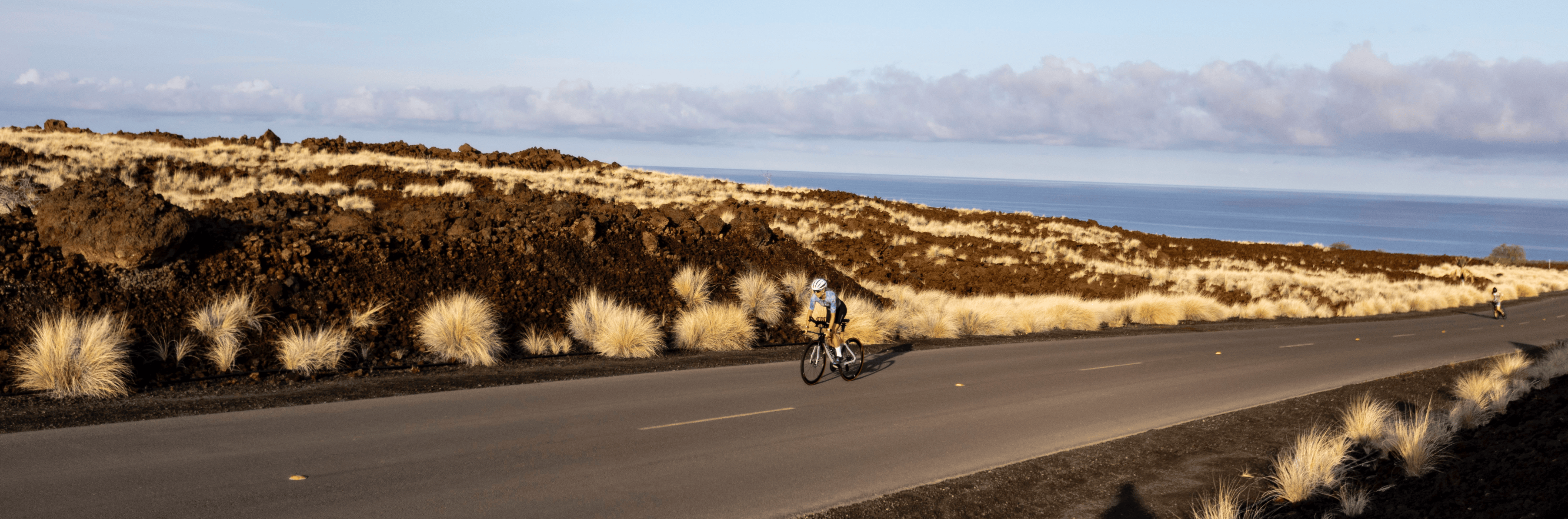 A triathlete climbing on an open road in Kona, HI with the ocean in the background