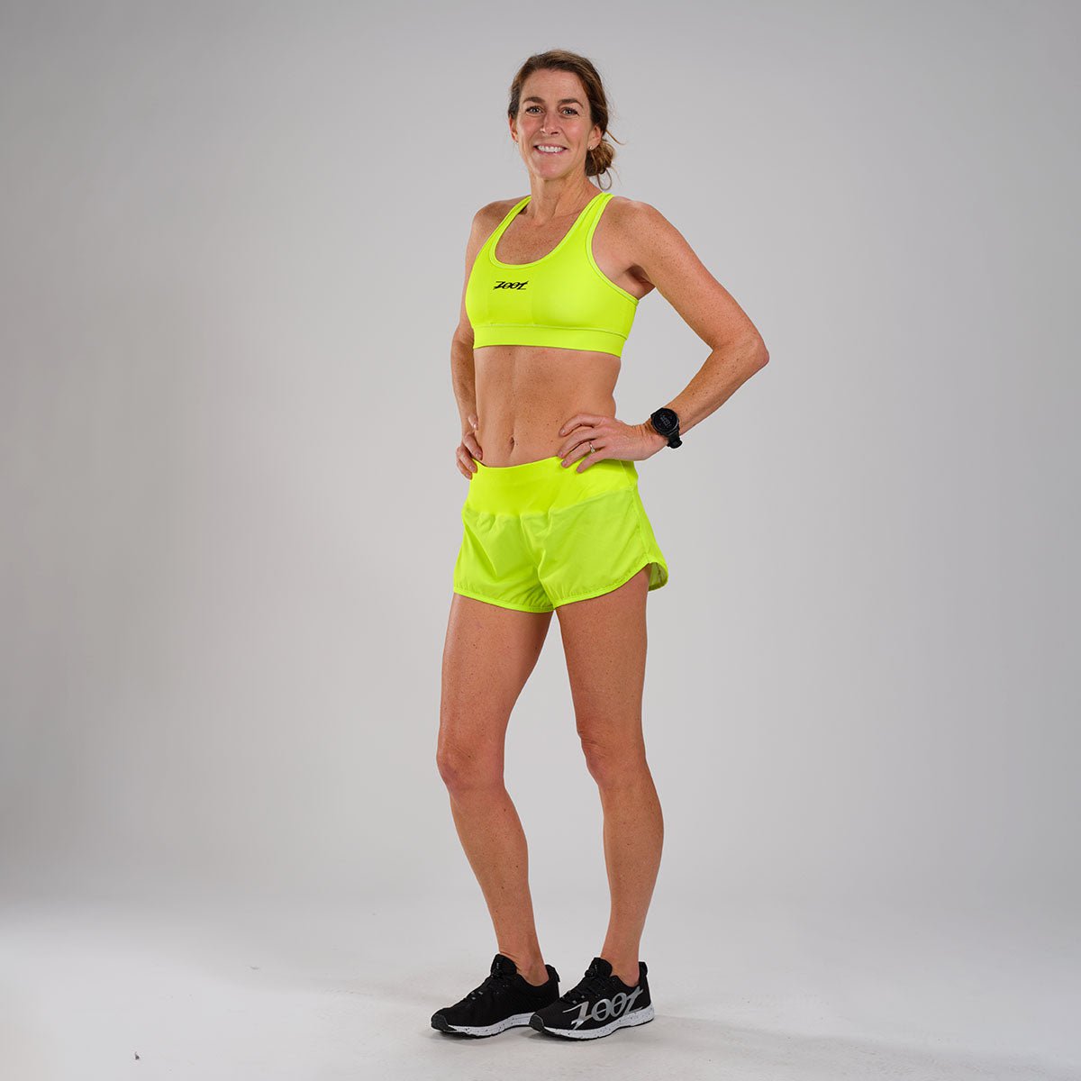 Female runner on beach with sports bra and shorts. Midsection closeup of  body of a woman athlete running with speed fast training cardio wearing  neon yellow activewear outfit. Active lifestyle. Stock Photo